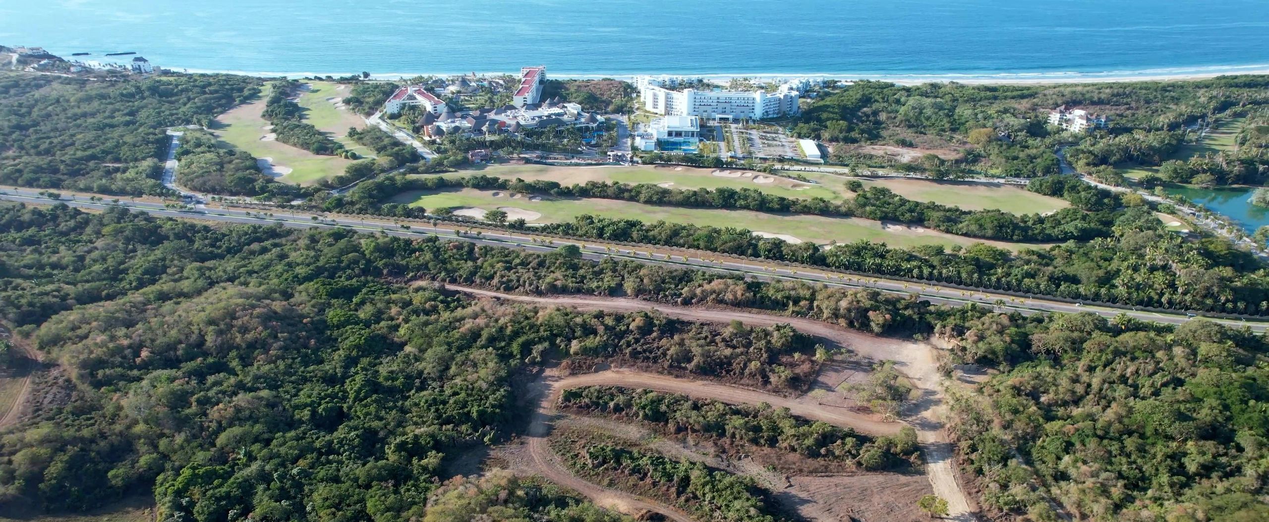 Vista aérea del terreno de Higuera Residence con Higuera Golf Club del otro lado de la carretera y el océano Pacífico al fondo